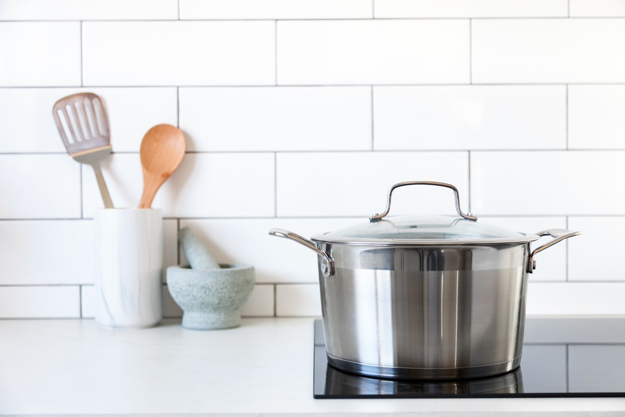 Large pot sits on an induction hob, with cooking utensils in the background against subway tile splashback.