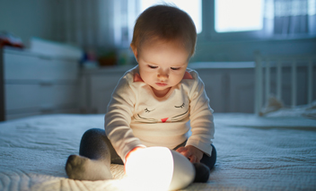 Baby plays with bedside lamp in nursery.