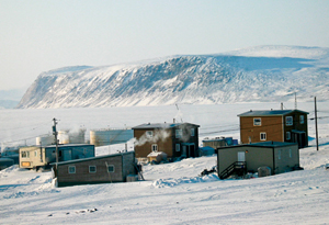 A winter photograph of several houses of Clyde River with mountainous snow covered terrain in the background
