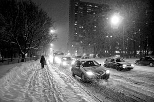nighttime photograph showing vehicles and pedestrian on snow covered Quebec City street