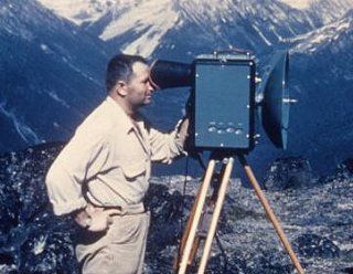 Technician looking through a tellurometer on a tripod with mountains in the background