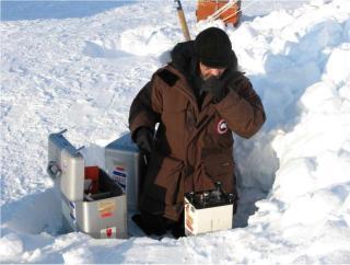 Technician kneeling taking gravity measurements on the snowy ground