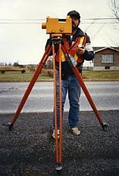Technician operating a level on a tripod on the shoulder of a road