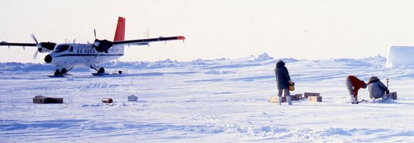 Technicians working with equipment in the snow with a grounded plane in the background