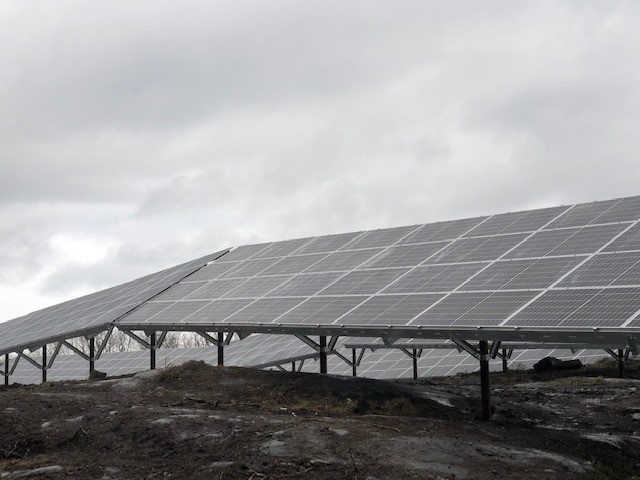 Several rows of solar panel arrays mounted on uneven rocky terrain.