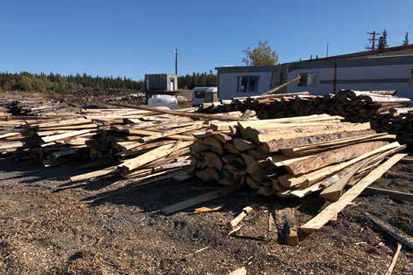 Timber yard containing long pieces of wood waste stacked in front of an industrial building.