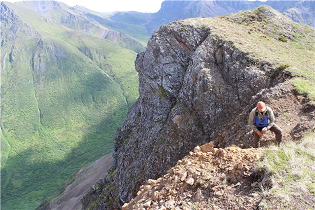 A photo of a geologist collecting samples of rocks in a mountainous range.