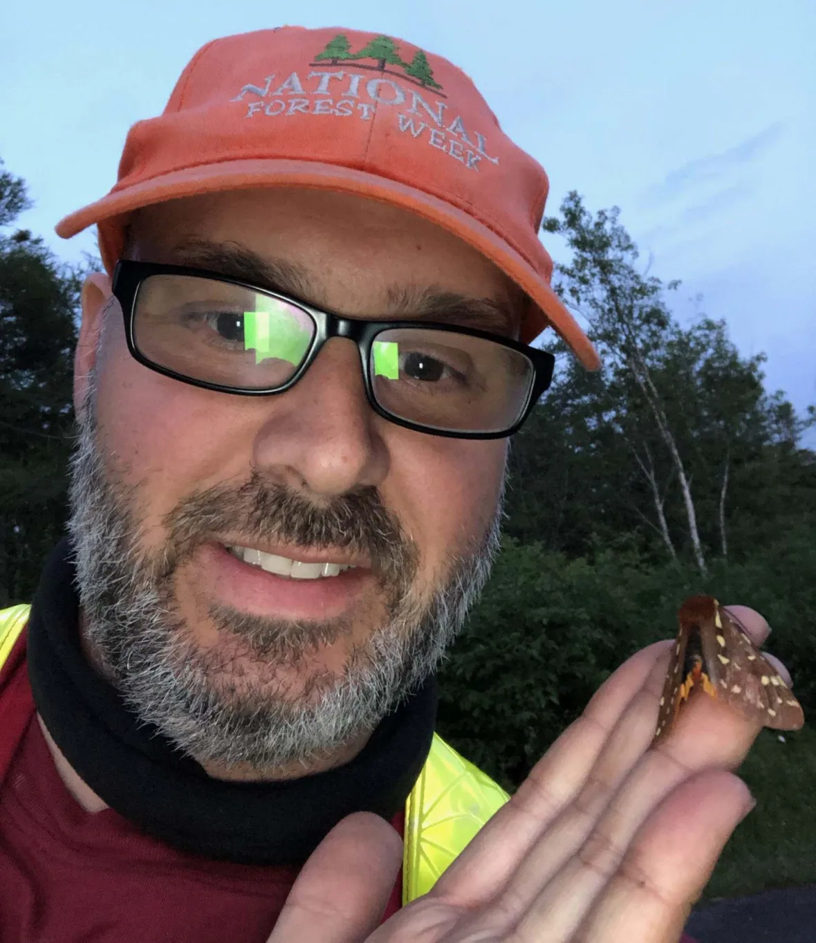 A close up of Joe wearing an orange cap with a moth in hand.