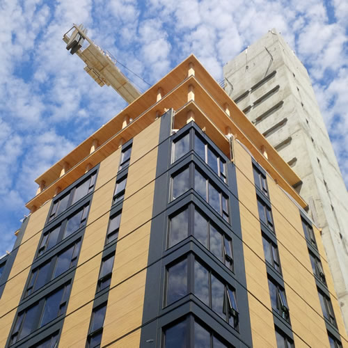 An 18-storey tall wood hybrid building in final stages of construction. Windows and siding partially finished and wooden floors and concrete column exposed.